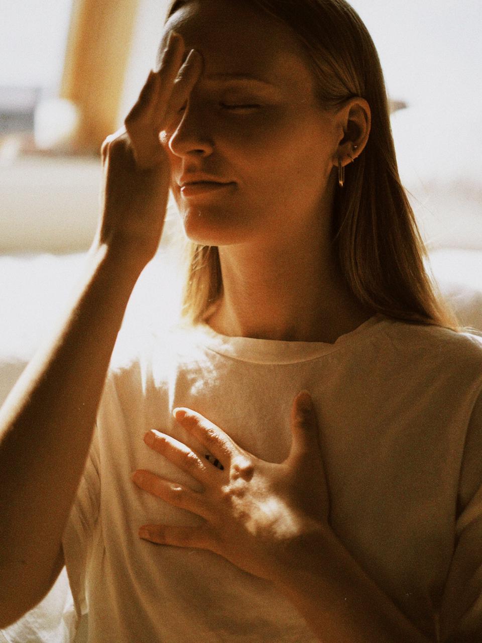 Matthäa with one hand on her chest, eyes closed in warm light