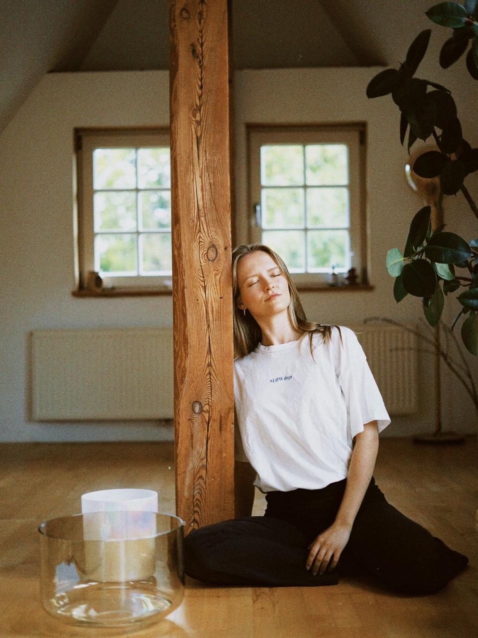 Matthäa resting against a wooden beam in her attic studio, singing bowls beside her